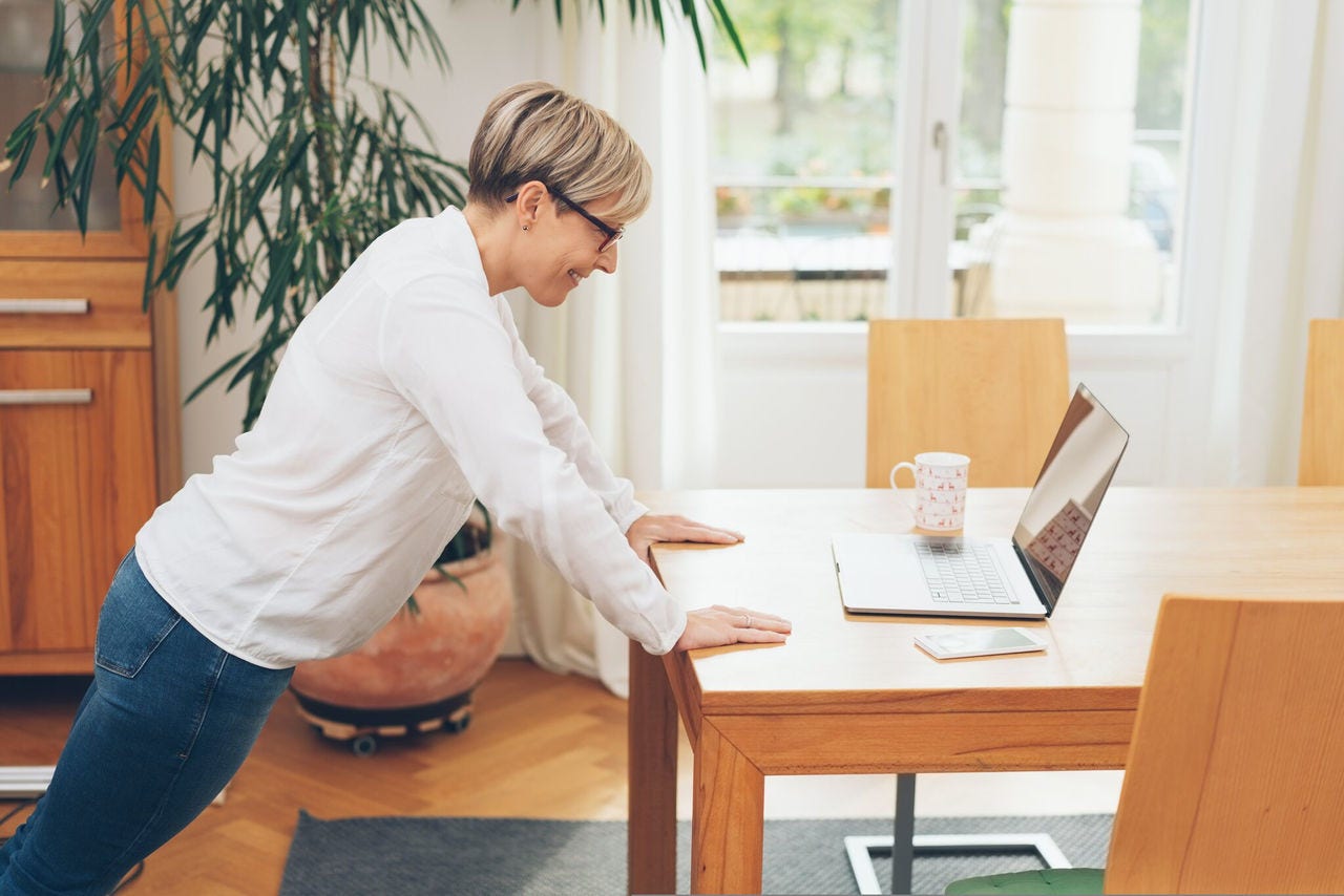 Person doing pushup at desk in front of laptop