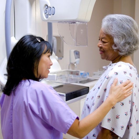 nurse preparing woman in hospital gown for mammogram