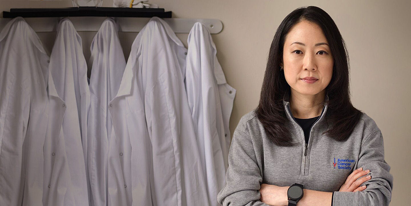 Mujer de pie junto a batas de laboratorio blancas colgadas.