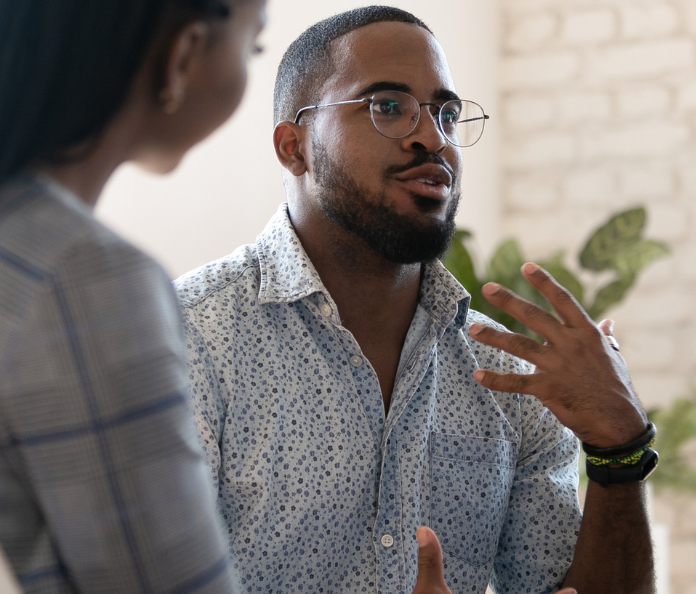 black man wearing glasses sitting talking to a group talking