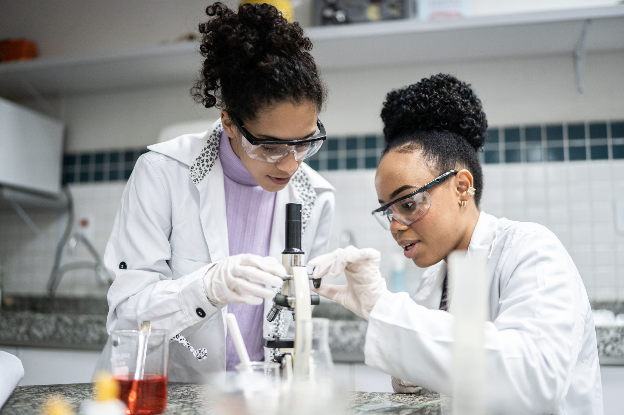 2 teenage Black students using the microscope in the laboratory