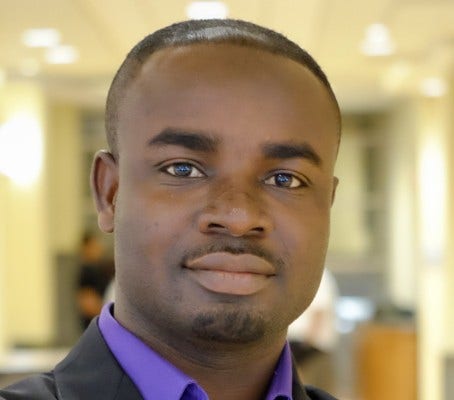 Young Black man with moustache and goatee, purple shirt, and dark suit jacket