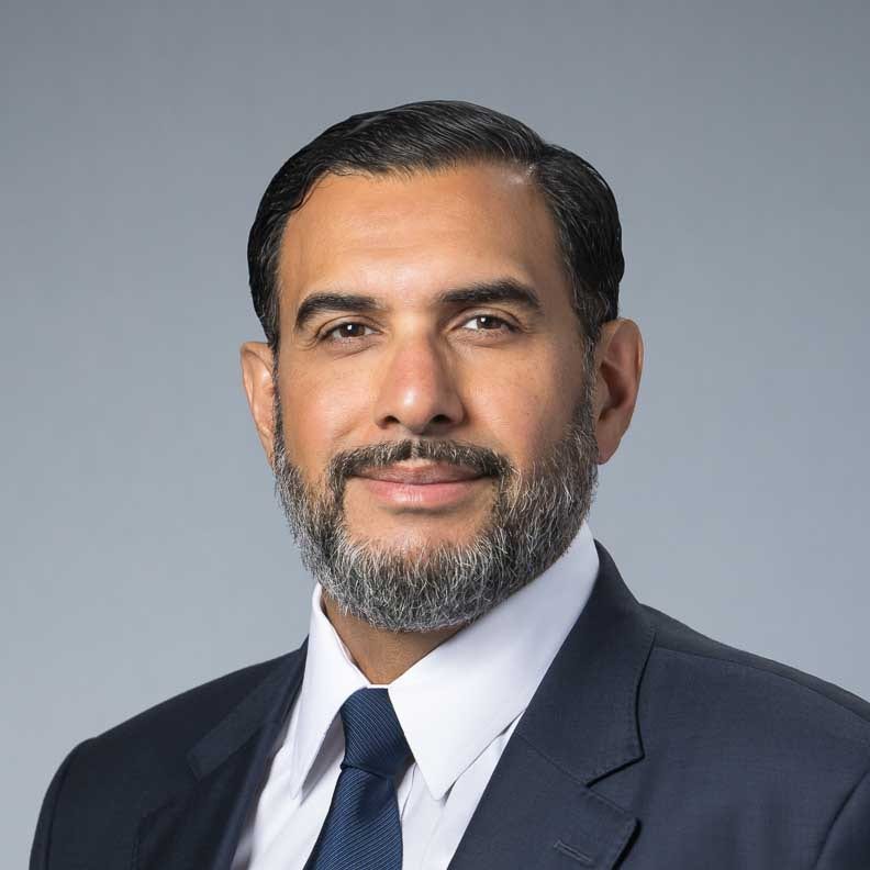 Professional man with beard wearing suit and tie, neutral background.
