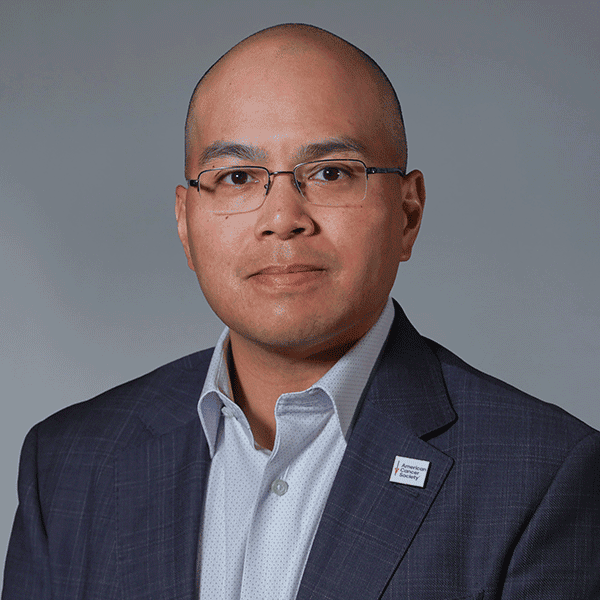 Man wearing glasses, a blazer, and an American Cancer Society pin.