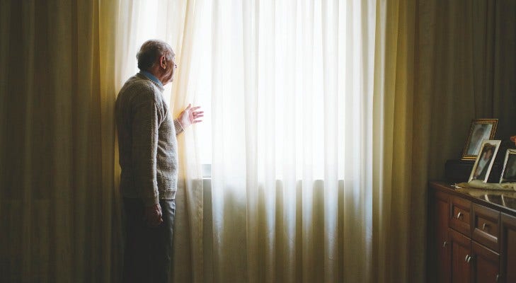 lone senior man looks out of his window