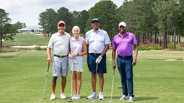 Four golfers posing together on a sunny golf course.