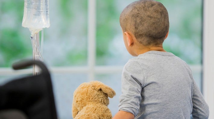 little boy with stuffed animal sits on hospital bed and gets chemotherapy