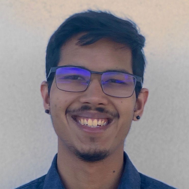Headshot of researcher Anuj Nanavati, MPH in a blue button-down shirt, black ear piercings, and black eyeglasses.