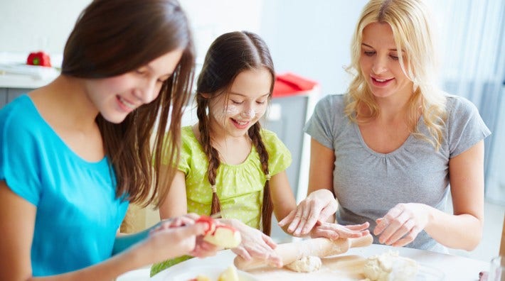 a young mother and her two daughters roll out dough for baking