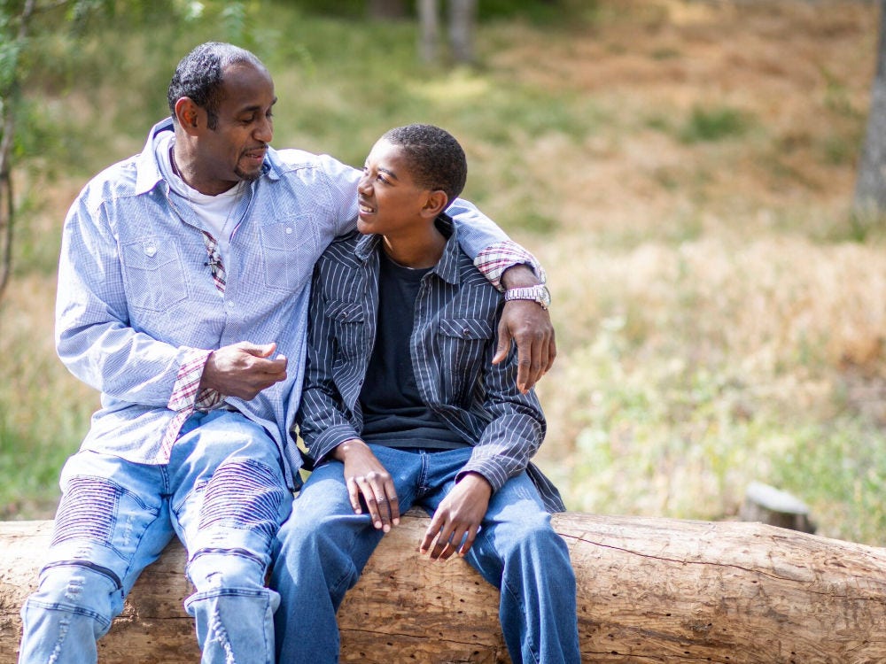 Image of a father and a son talking outside sitting on a log