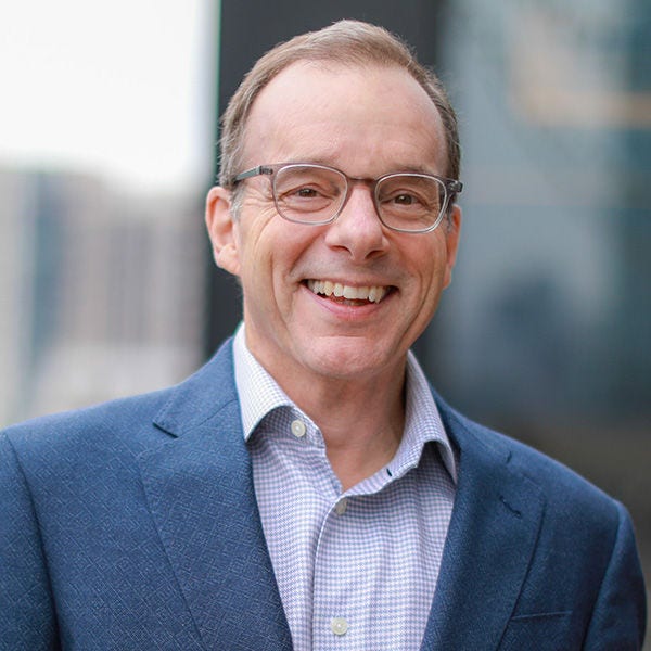 Smiling man wearing glasses and blue blazer outdoors.