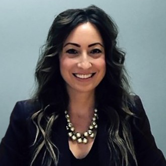 Professional headshot of a person wearing a dark blazer and necklace against a gray background.