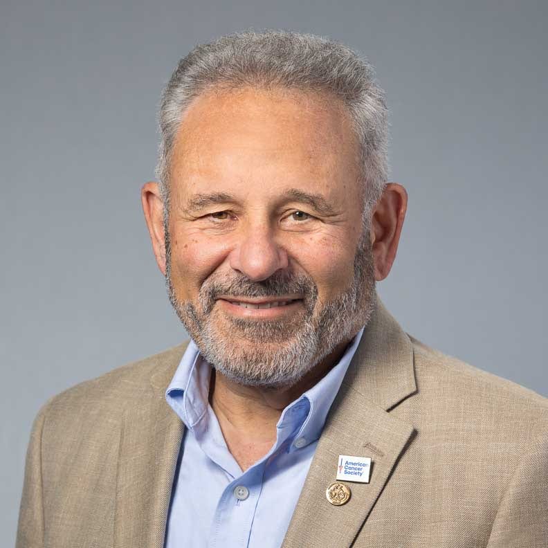 Smiling man in tan blazer with American Cancer Society pin.