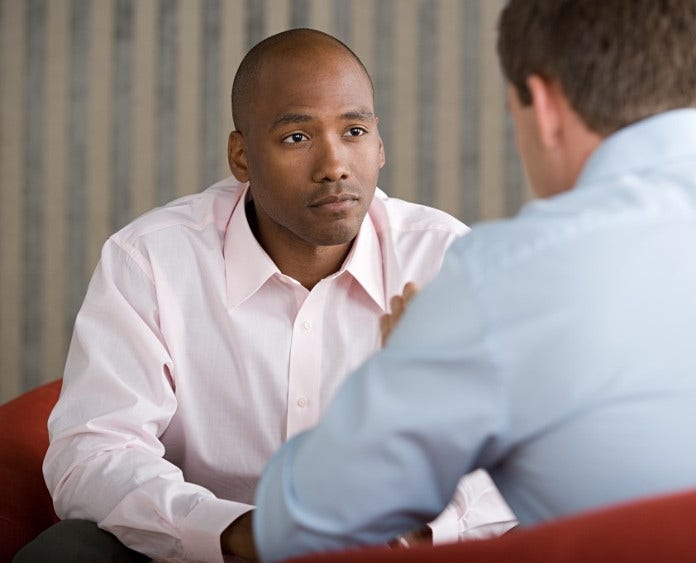 a concerned young man sits across from another man and listens as he talks