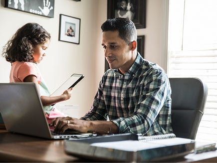 Man working on a laptop while a child holds a smartphone.