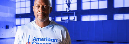 NBA star Alonzo Mourning posing for photo inside of basketball court with American Cancer Society Shirt on