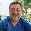 Hombre sonriente con camisa azul sentado al aire libre.