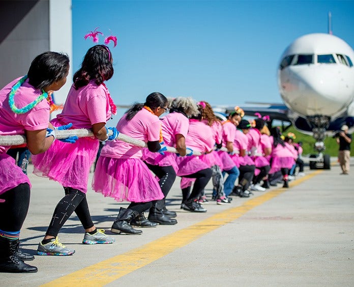 Ladies Delta Jet Drag Team wearing pink tutus and pulling a Delta airplane with a heavy rope