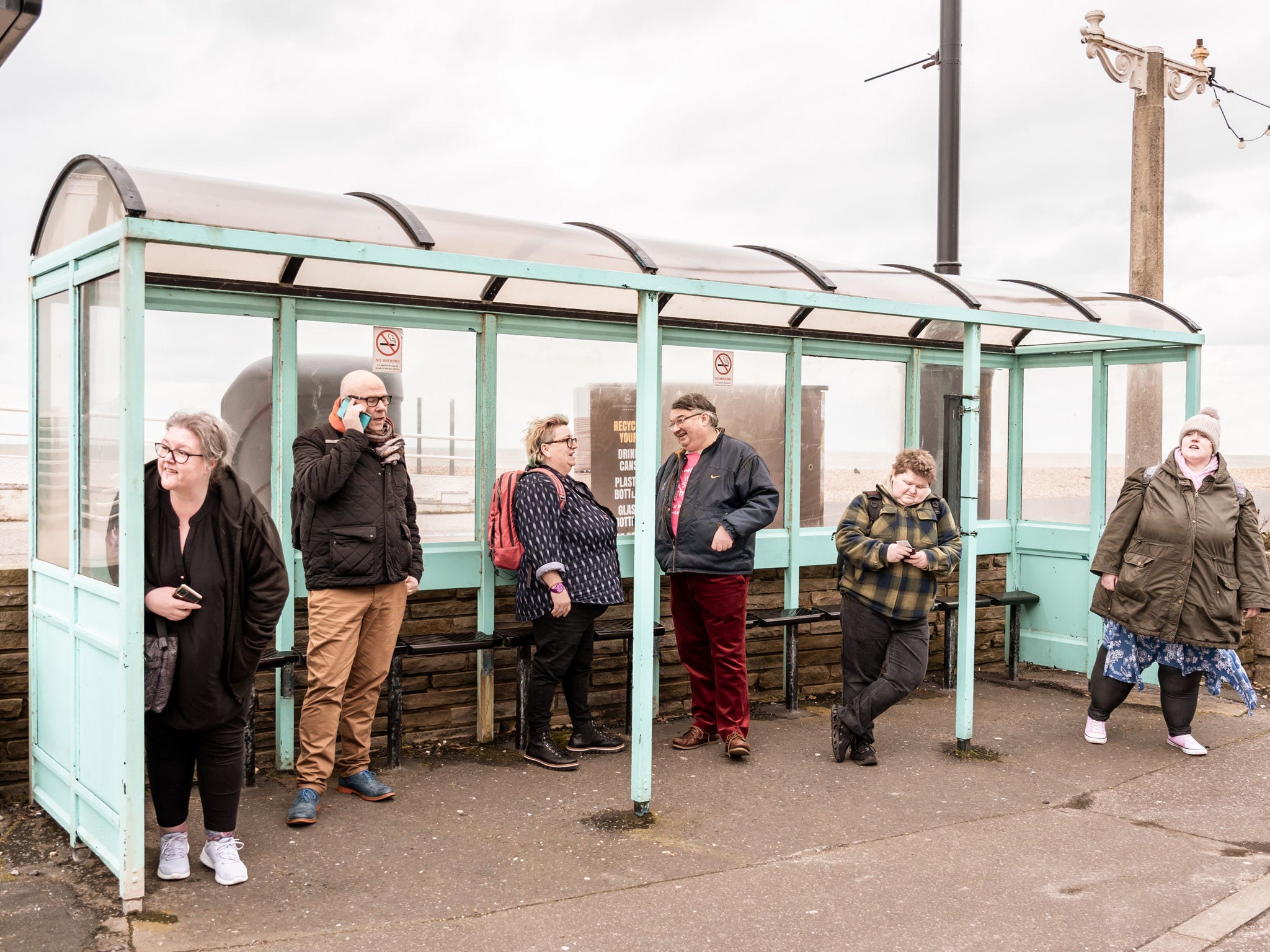 People in coats standing under light blue bus stop