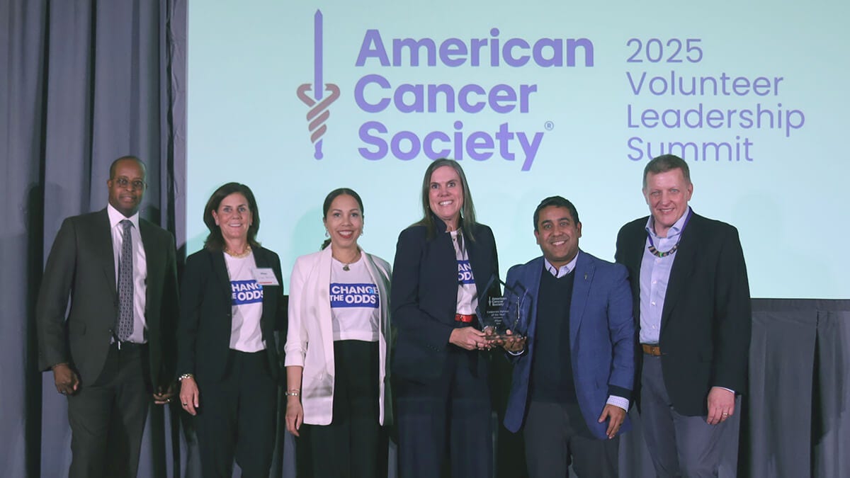 Seven people posing with award at conference stage backdrop.