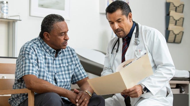 doctor goes over a chart with a male patient in exam room