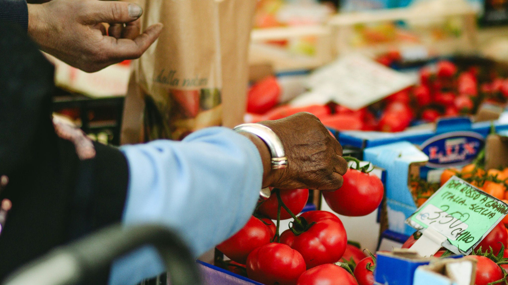 black hand with bracelet, light blue jacket picking up tomato