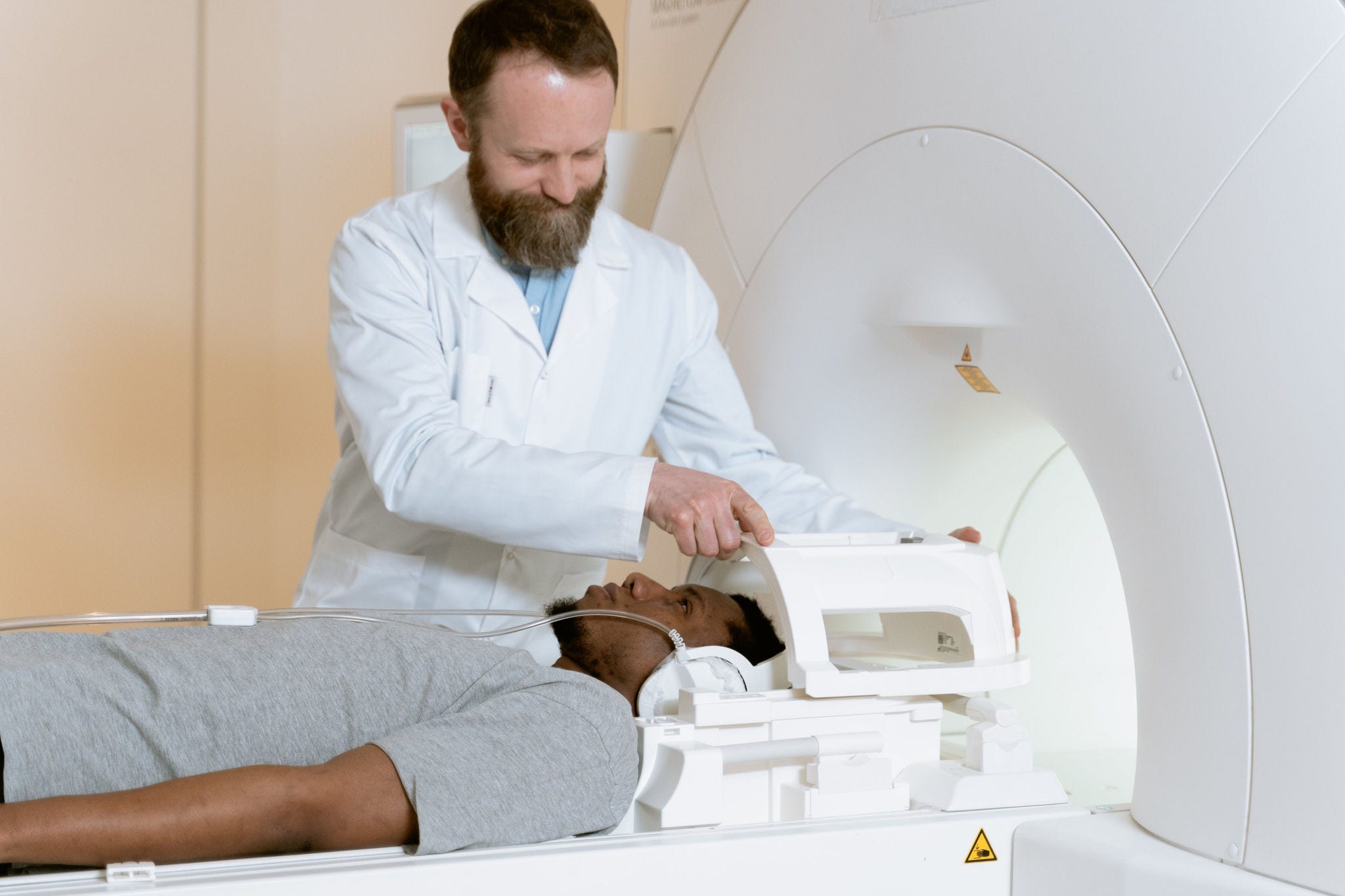 bearded tech putting something near head of black bearded man about to enter ct scan 