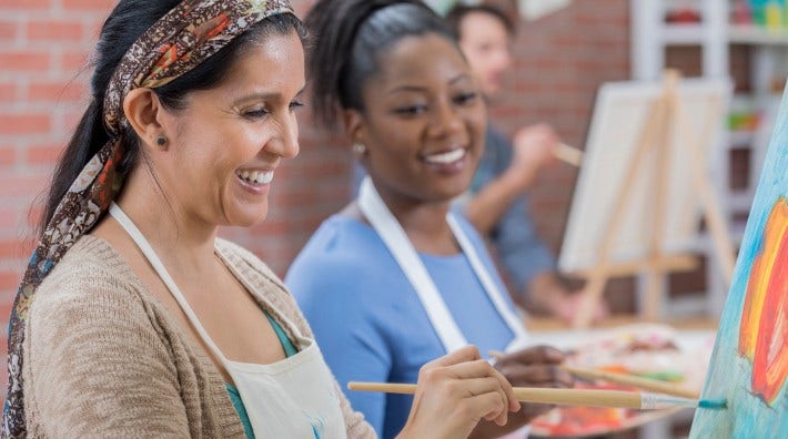 two women painting on canvas in art class