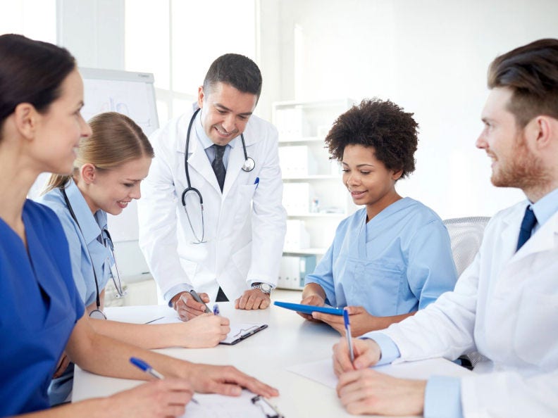A group of health care professionals gathered around a table writing on clipboards. 