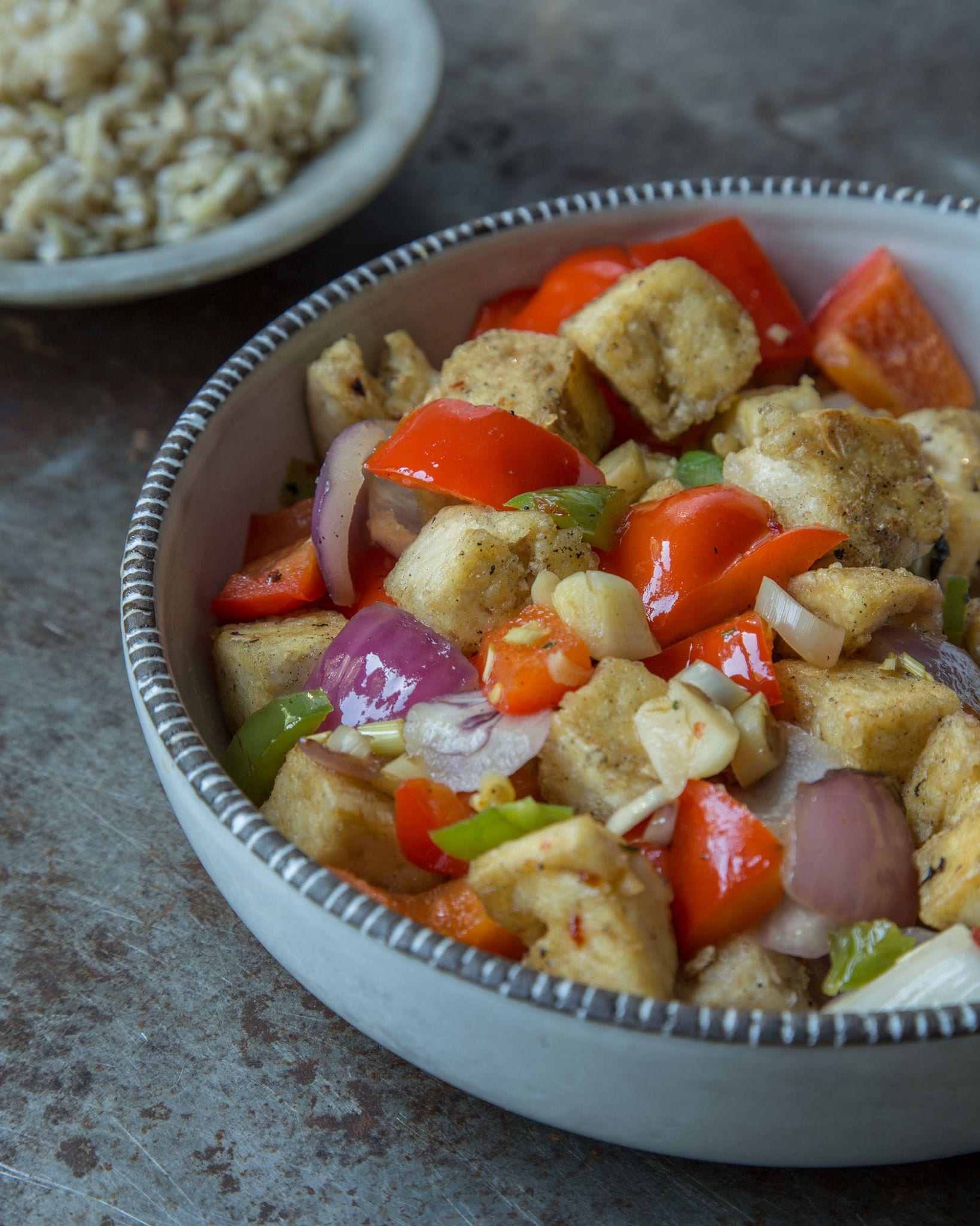 A closeup shot shows crispy tofu with lemongrass and peppers in a light blue bowl.