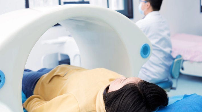 A woman in a yellow shirt gets a bone scan, while a man wearing a lab coat sits next to the bone scanning machine. 