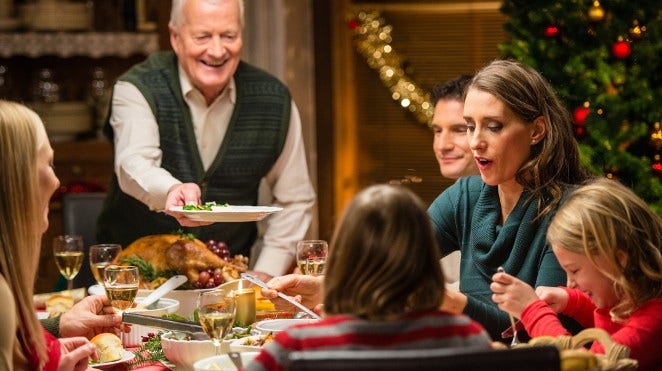 grandfather serves carved turkey to his family at Christmas dinner table