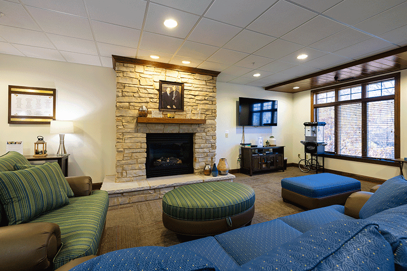 Cozy lounge with stone fireplace, couches, TV, and windows.