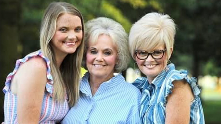 Three women standing together outdoors, smiling.
