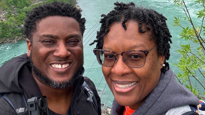 Pareja sonriendo para una selfie junto a un río de aguas turquesas.