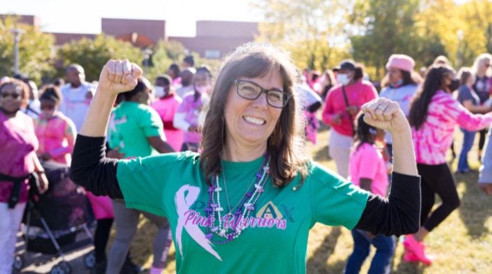 Woman with green shirt and brown hair smiles while flexing bicep muscles at a cancer awareness event