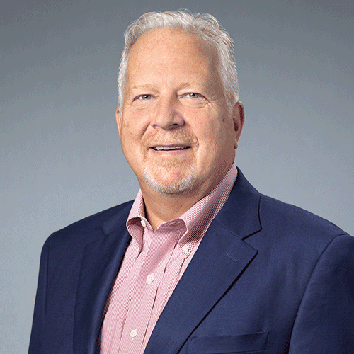 Smiling man with gray hair, navy blazer, pink shirt.