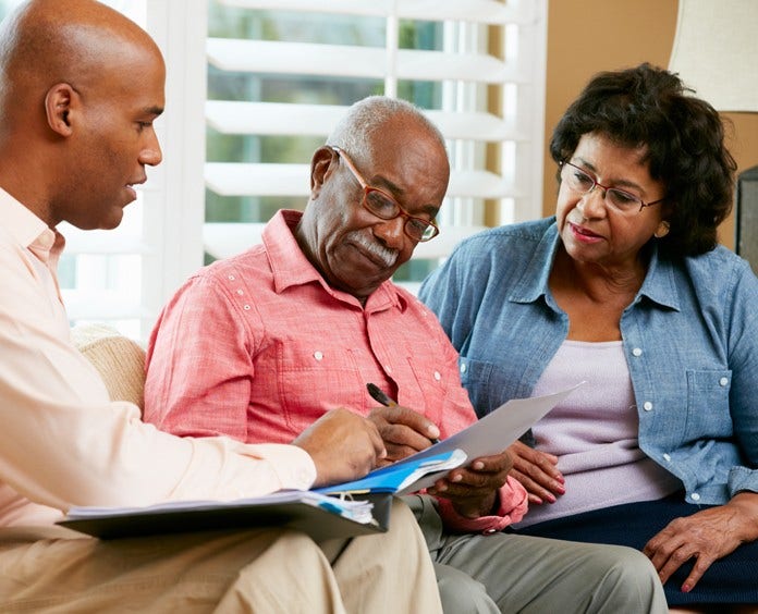 Financial Advisor Talking To Senior Couple At Home Signing Documents Sitting On Sofa