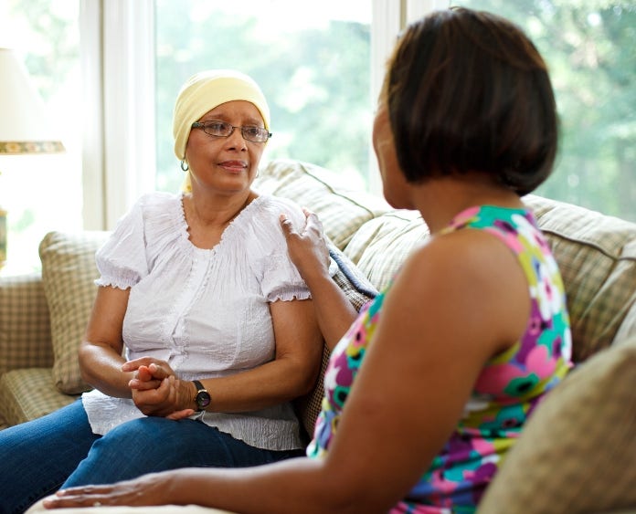 a woman comforts a female cancer patient in head scarf  