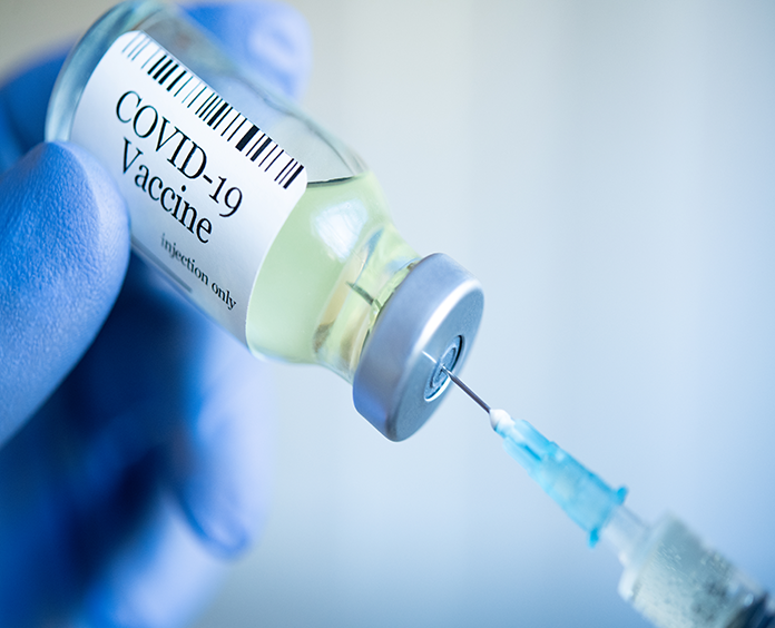 Blue gloved hand holding bottle with clear liquid labeled COVID-19 Vaccine with syringe needle inserted into it 