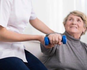 physical therapist helps a senior woman lift weights