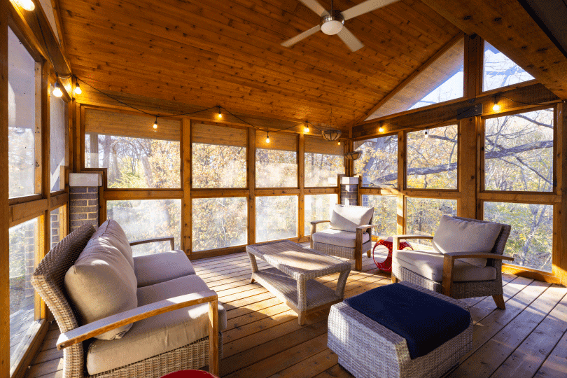 Sunlit wooden screened porch with wicker seating and string lights.