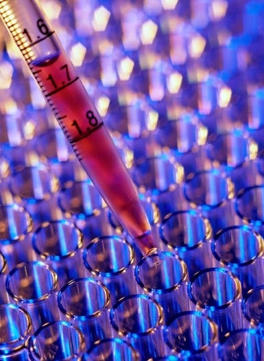 a dropper drops colored liquid into test tubes in lab