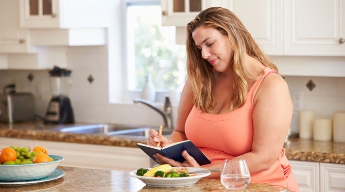 woman sitting at kitchen counter writing in her food diary