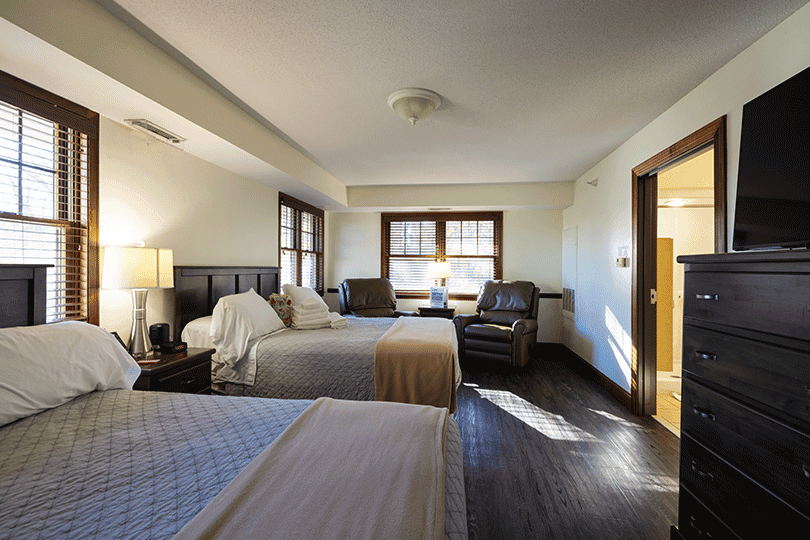 Bedroom with two beds, chairs, dresser, and bathroom doorway.