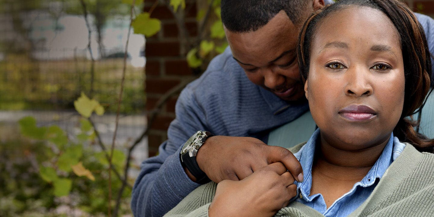 Hombre abrazando a una mujer sentada al aire libre con un suéter verde.
