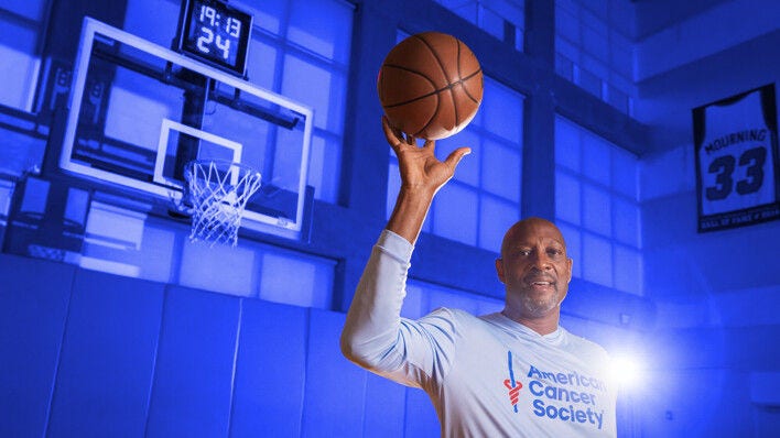 Alonzo Mourning holding a basketball in an American Cancer Society Shirt