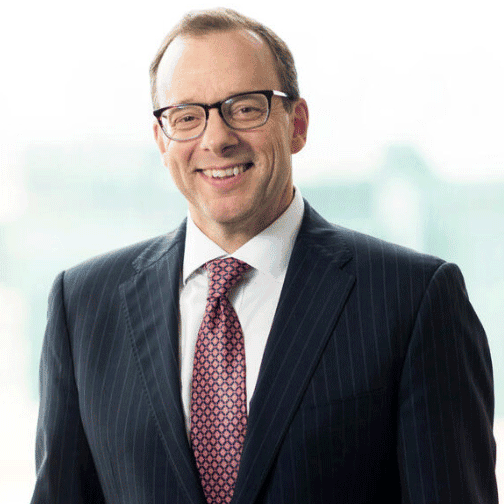 A man in a dark pinstripe suit and patterned tie smiling at the camera.