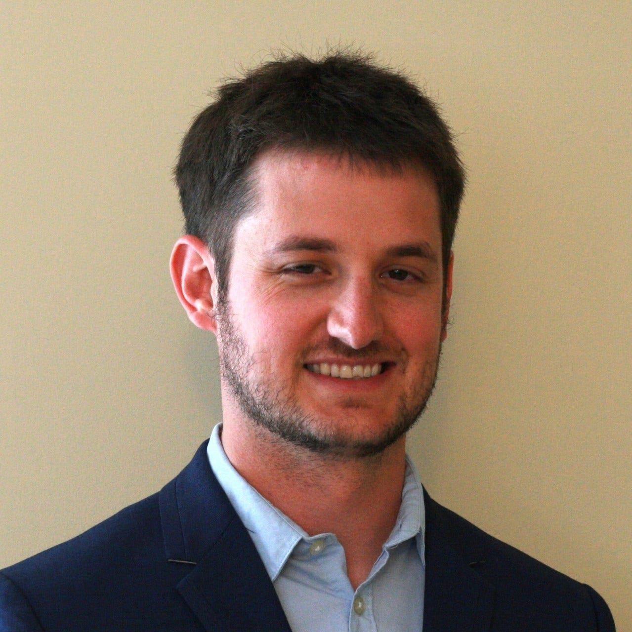 man with dark hair, moustache, and beard in blue button-down shirt and blue jacket