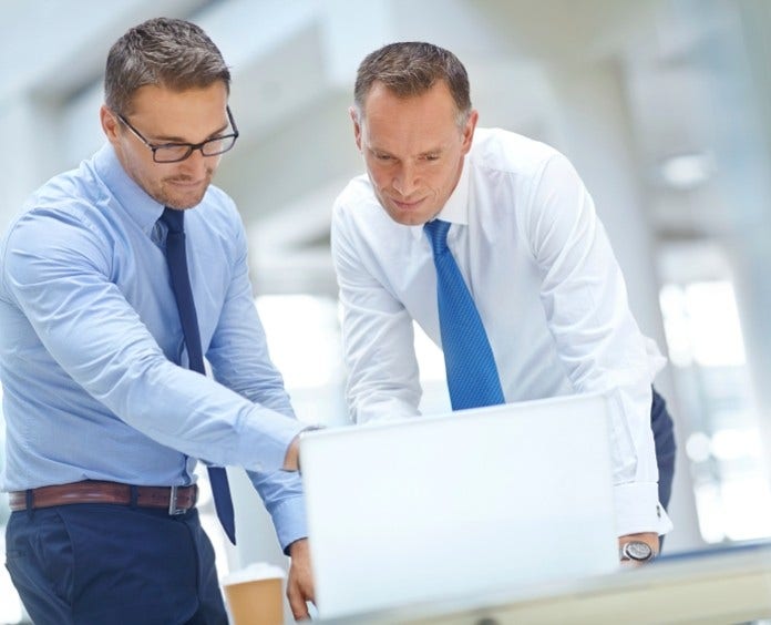 two men standing and working in front of a computer in an office setting